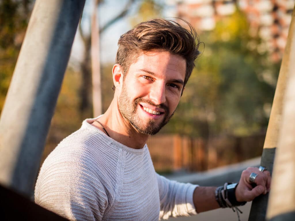 One handsome young man in urban setting in European city, standing and smiling to camera happy